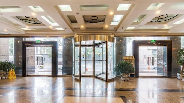 Een hotellobby met een draaideur, grote ramen en een gepolijste marmeren vloer.