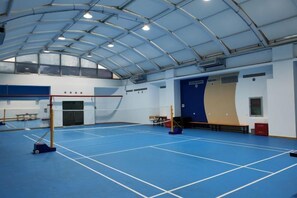 Un gimnasio interior con suelo azul, aro de baloncesto y pared de escalada.