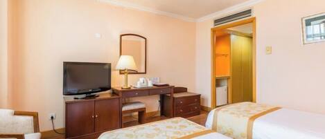 Habitación de hotel con dos camas, un escritorio con televisión, un espejo y un armario.