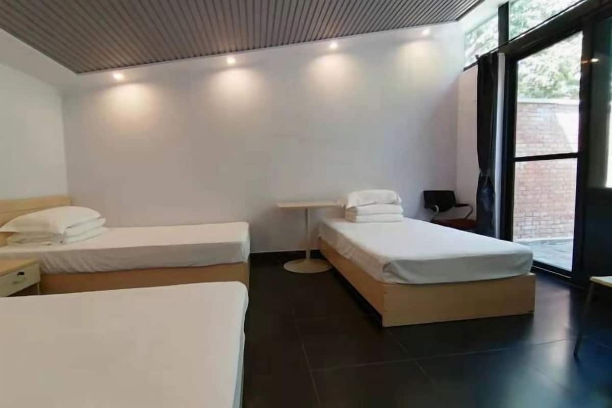 A modern hotel room with two beds, a bedside table, a lamp, and a large window.
