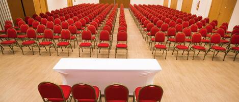 Un salón de conferencias con filas de sillas rojas y una mesa blanca en el centro.