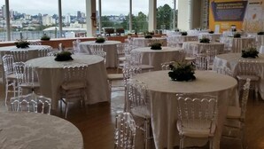 A banquet hall with round tables and chairs, large windows with a city view, and banners on the walls.