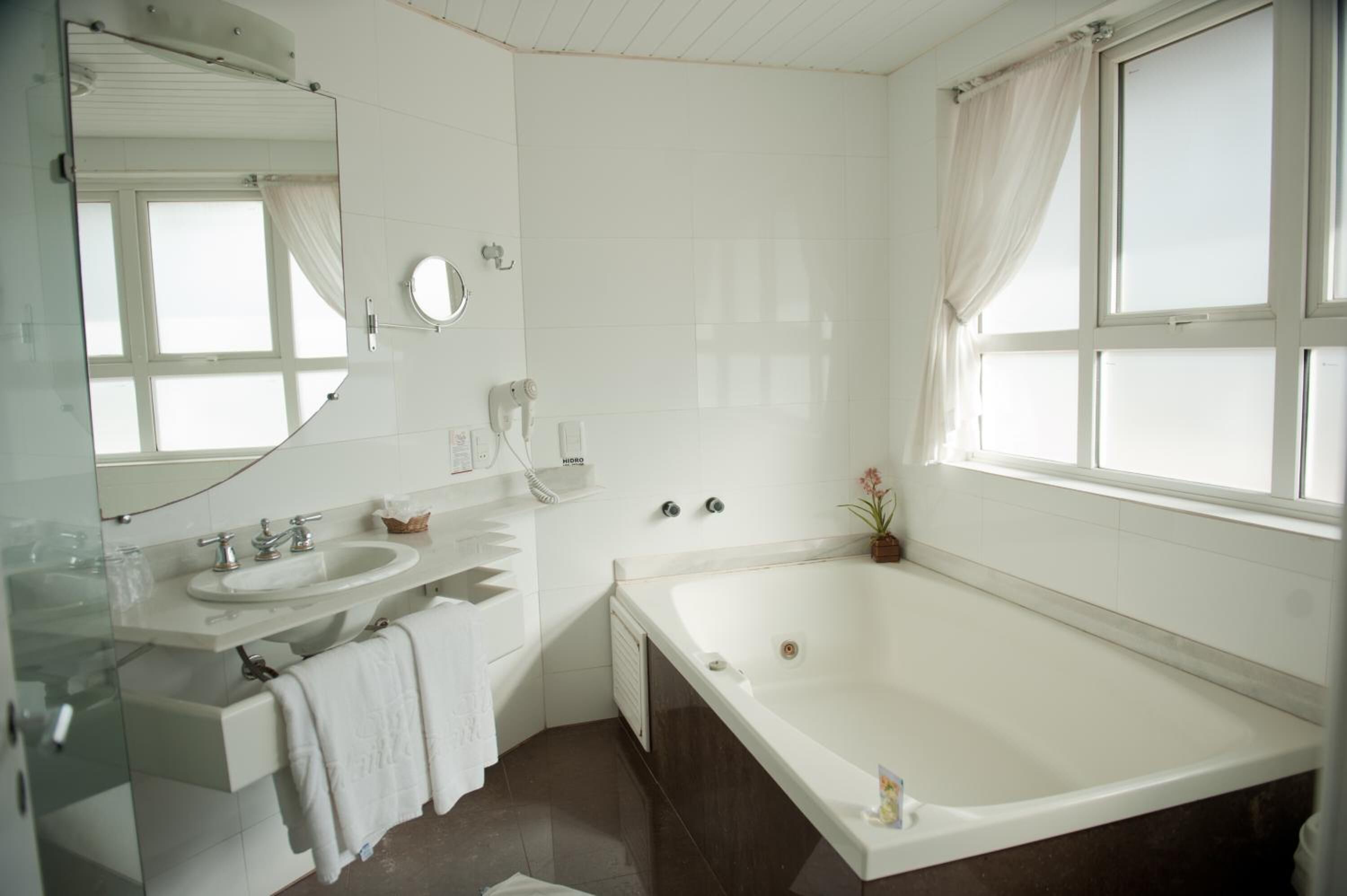Une salle de bain moderne avec une grande baignoire, un meuble-lavabo avec un miroir et une fenêtre avec des rideaux.