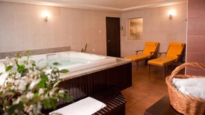 A spa room with a hot tub, two yellow chairs, a wooden bench, and a basket with towels.