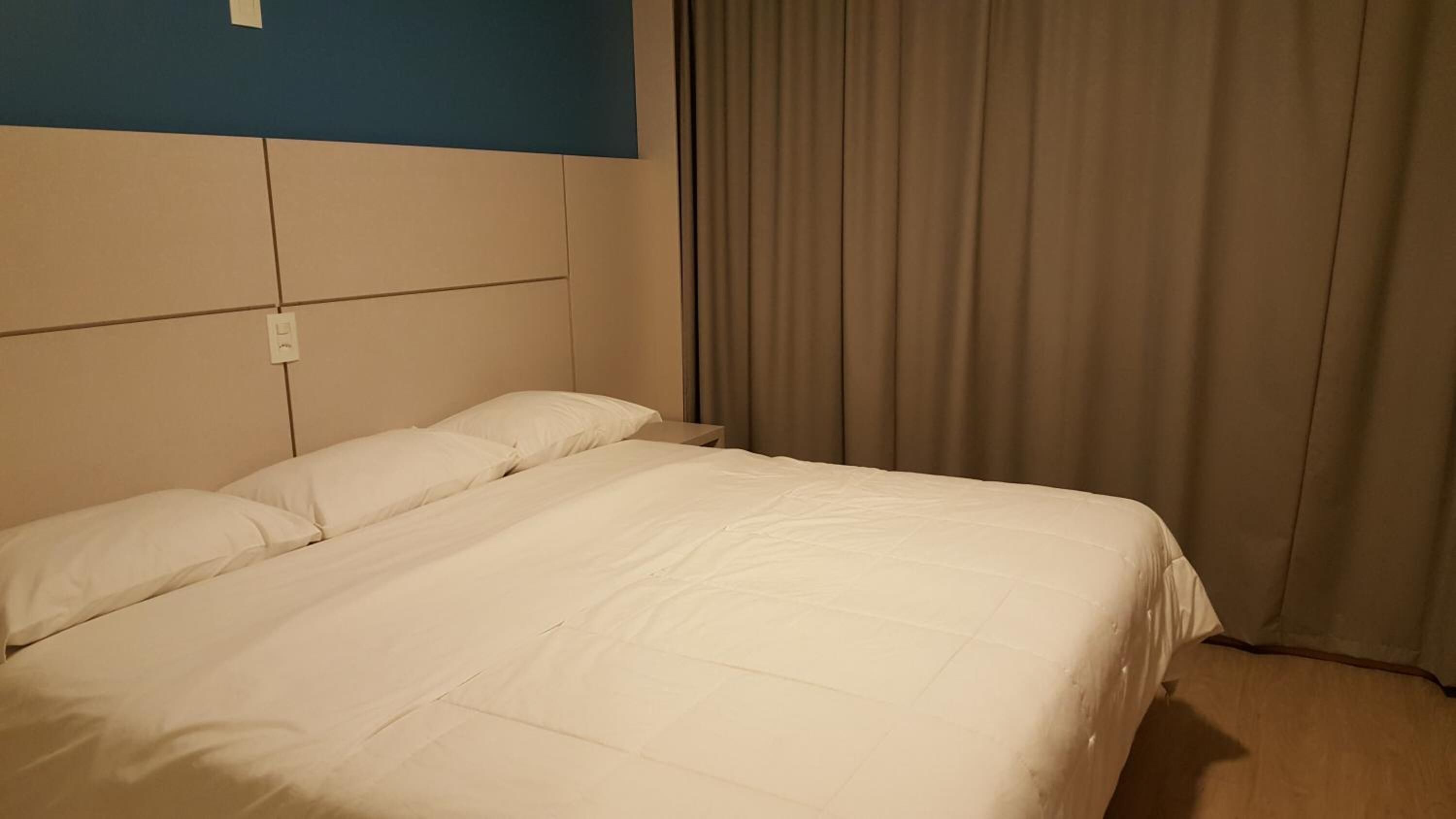 A hotel room with a large bed, a headboard, a nightstand, and a window with curtains.