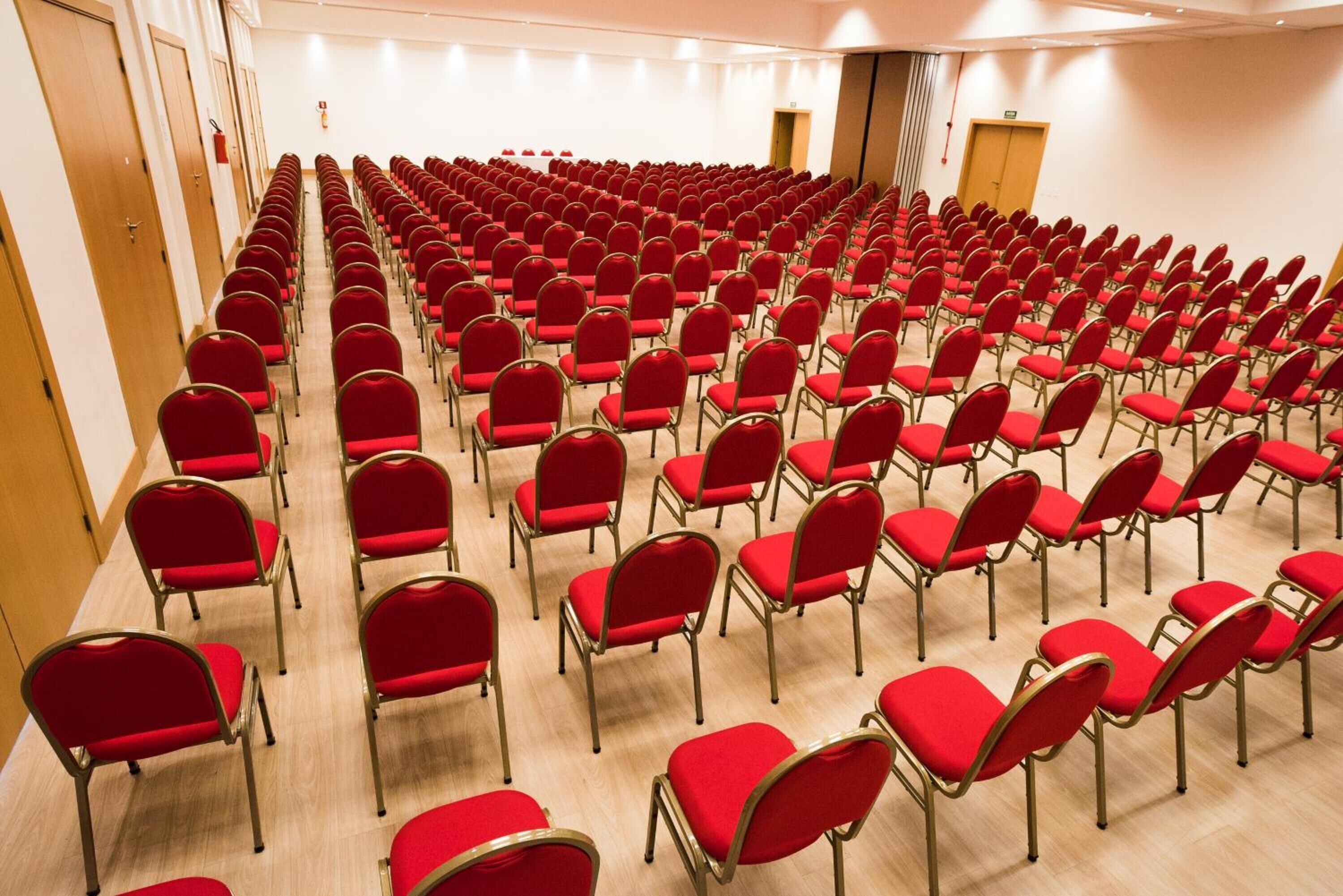 Un salón de conferencias con filas de sillas rojas y suelo de madera.