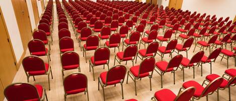 Un salón de conferencias con filas de sillas rojas y suelo de madera.
