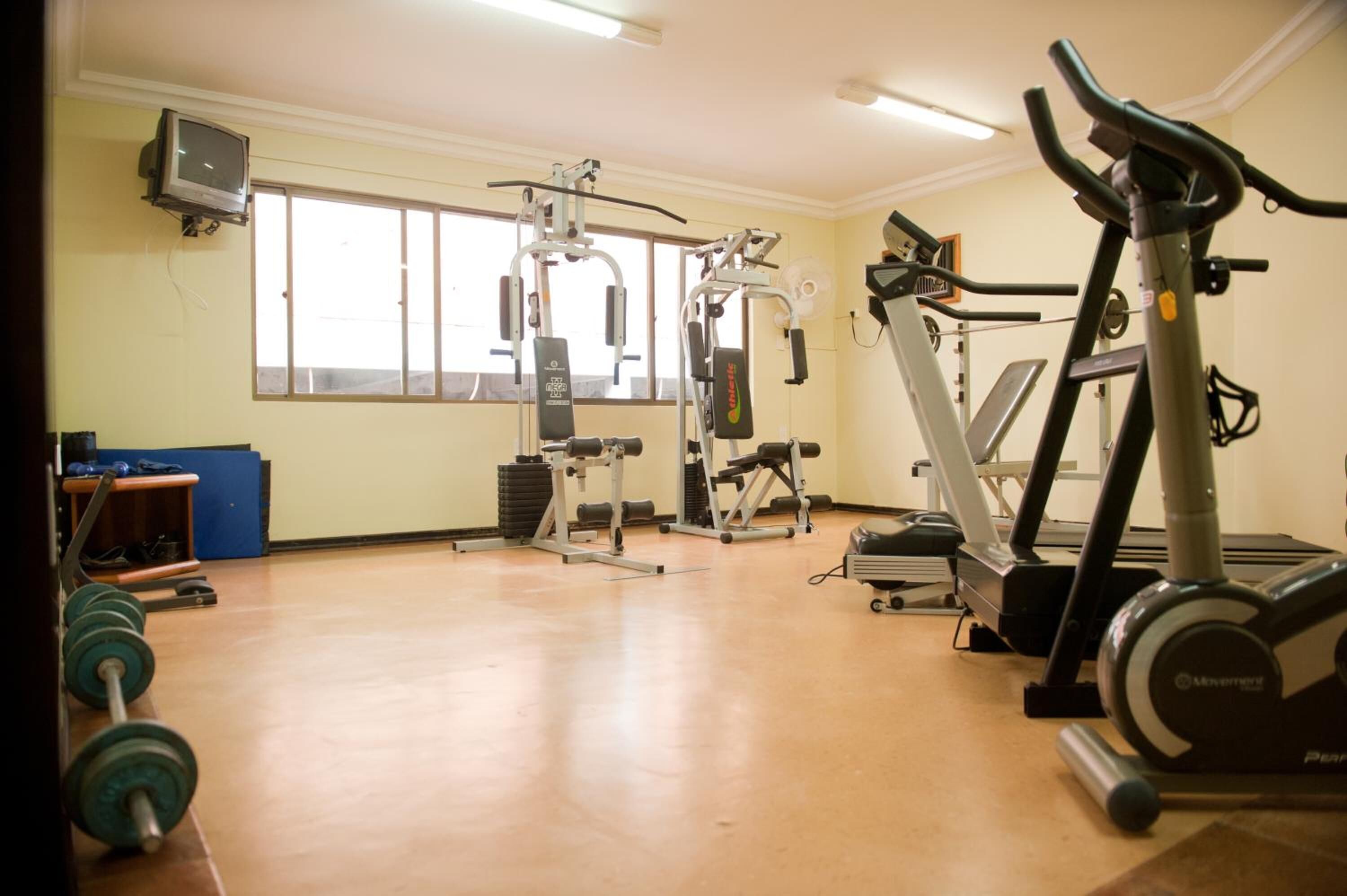 Uma academia com equipamentos de cardio, aparelhos de musculação e uma televisão na parede.
