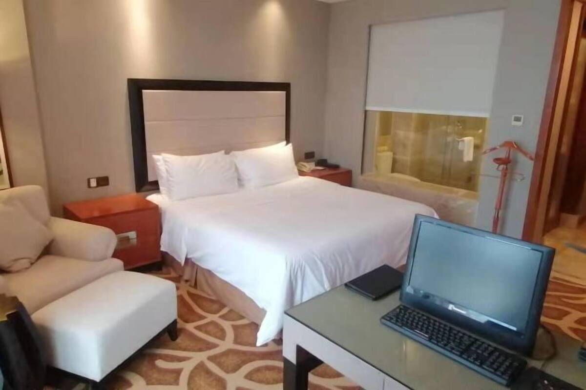 Une chambre d’hôtel comprenant un lit, un bureau avec un ordinateur portable, une chaise, une table de chevet et une fenêtre avec des stores.