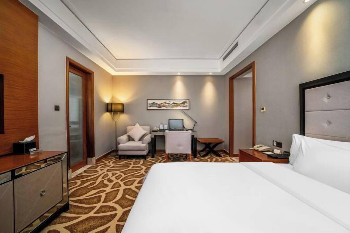 Une chambre d’hôtel avec un grand lit, un bureau avec un ordinateur, une chaise, une lampe de bureau et un téléphone.