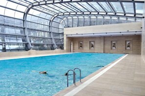 Una piscina interior con techo de cristal, suelo de madera y cuadros en las paredes.