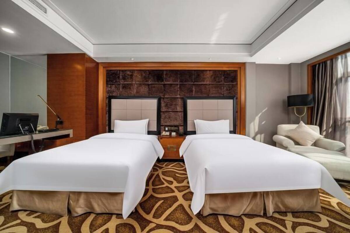 Une chambre d’hôtel avec deux lits, un bureau avec un ordinateur, une télévision et un canapé.