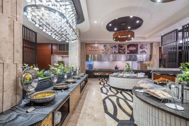 Une cuisine d’hôtel moderne, dotée d’un système de service de repas en buffet, d’appareils électroménagers en acier inoxydable et d’un éclairage décoratif.