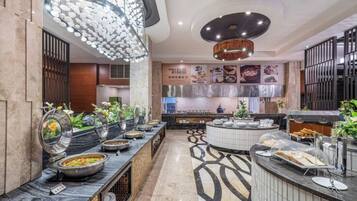 Une cuisine d’hôtel moderne, dotée d’un système de service de repas en buffet, d’appareils électroménagers en acier inoxydable et d’un éclairage décoratif.