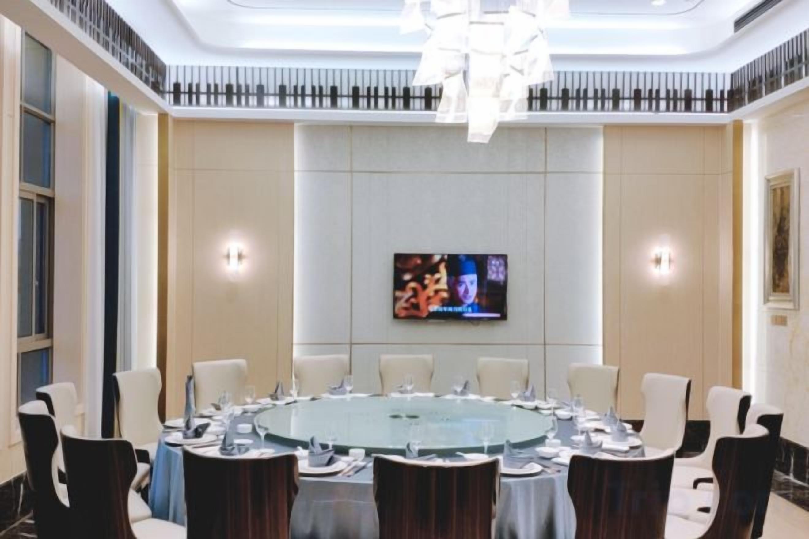 Un salón de conferencias con una mesa redonda, sillas, una pantalla de televisión y una lámpara de araña moderna.