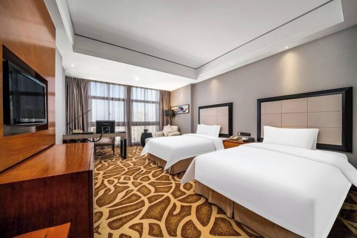 Une chambre d’hôtel avec deux lits, une télévision, un bureau et une grande fenêtre.