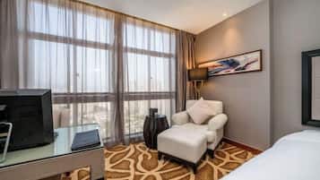 A hotel room with a large window, a desk with a computer, a chair, and a bed.
