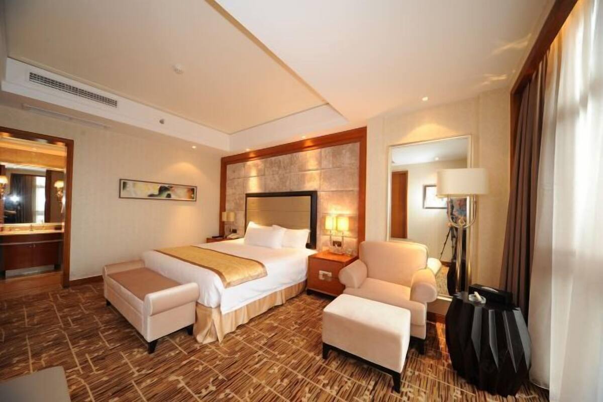 Une chambre d’hôtel avec un grand lit, un coin salon, un bureau et un miroir.