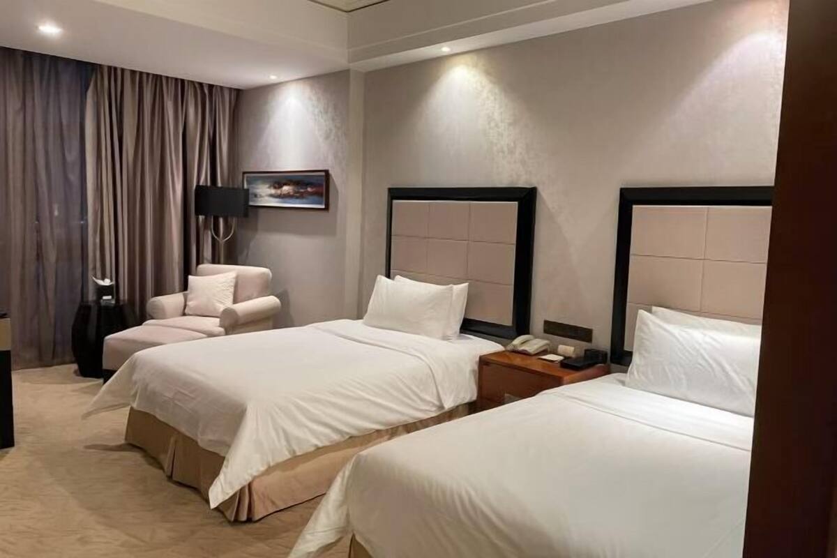 Une chambre d’hôtel avec deux lits, une chaise, une lampe et un tableau au mur.