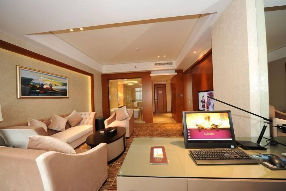 Une chambre d’hôtel équipée d’un canapé, de fauteuils, d’un bureau avec un ordinateur portable et d’une télévision.