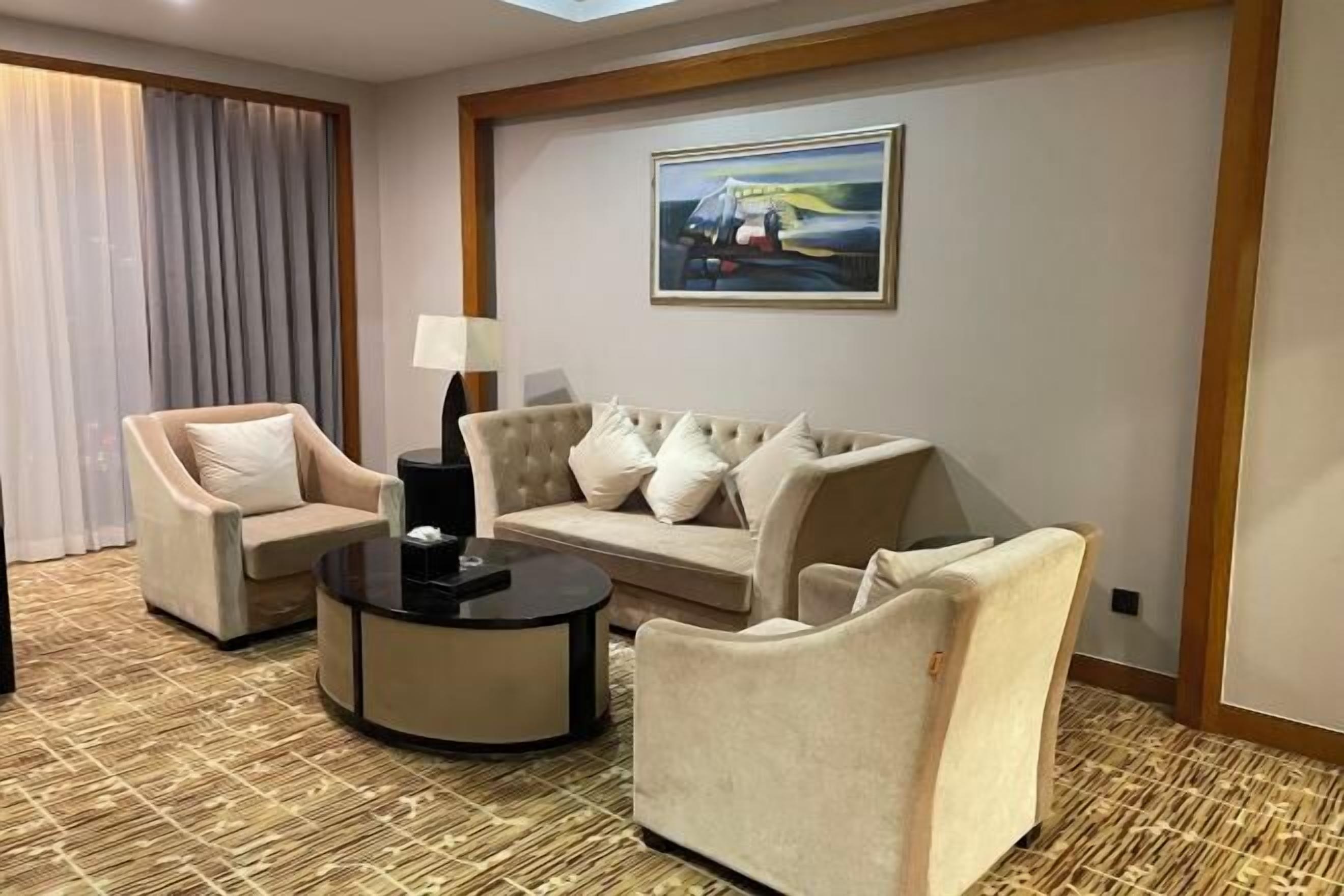 Ein Hotelzimmer mit einem beigefarbenen Sofa, zwei Sesseln, einem schwarzen Couchtisch und einem Bild an der Wand.