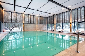 An indoor swimming pool with clear glass walls, lounge chairs, and a view of a snowy landscape. - Eva Park Life Spa (Konstancin-Jeziorna)