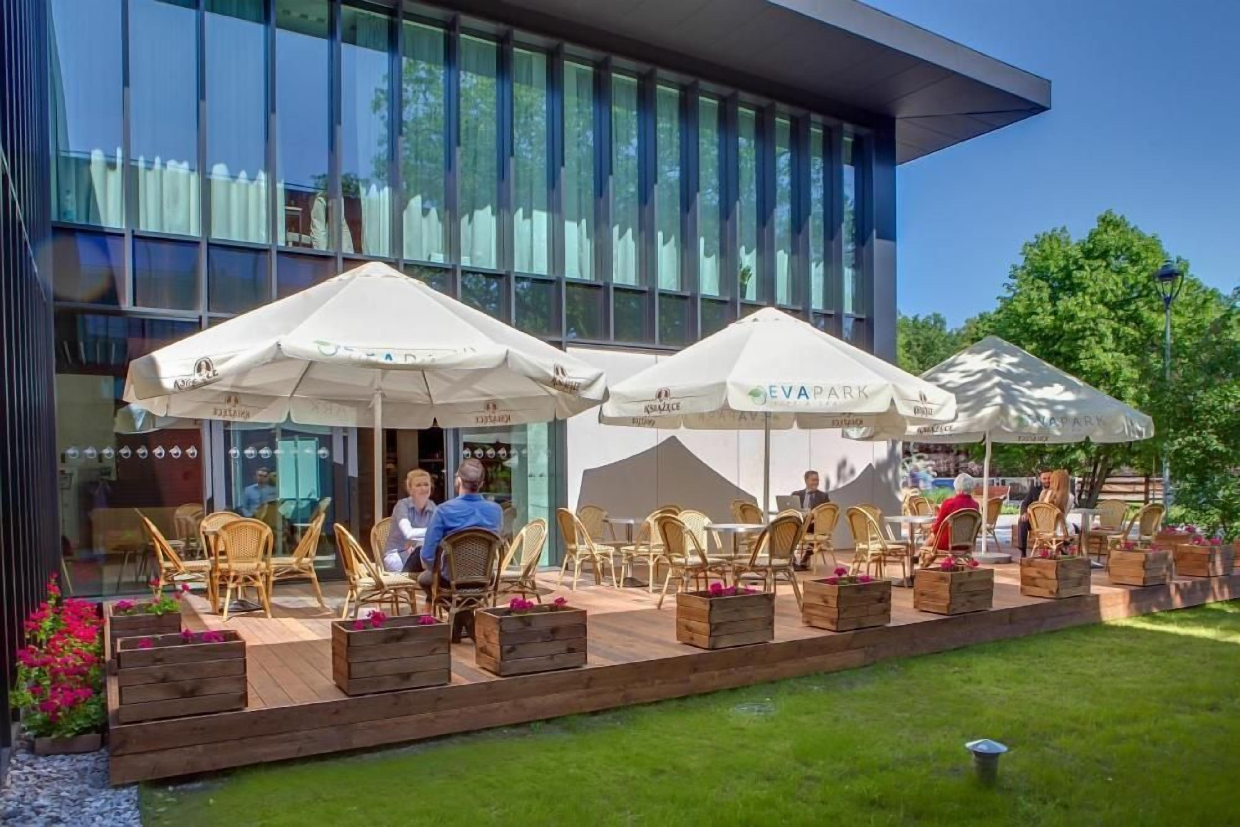 An outdoor seating area with white umbrellas, wicker chairs, and wooden planters.