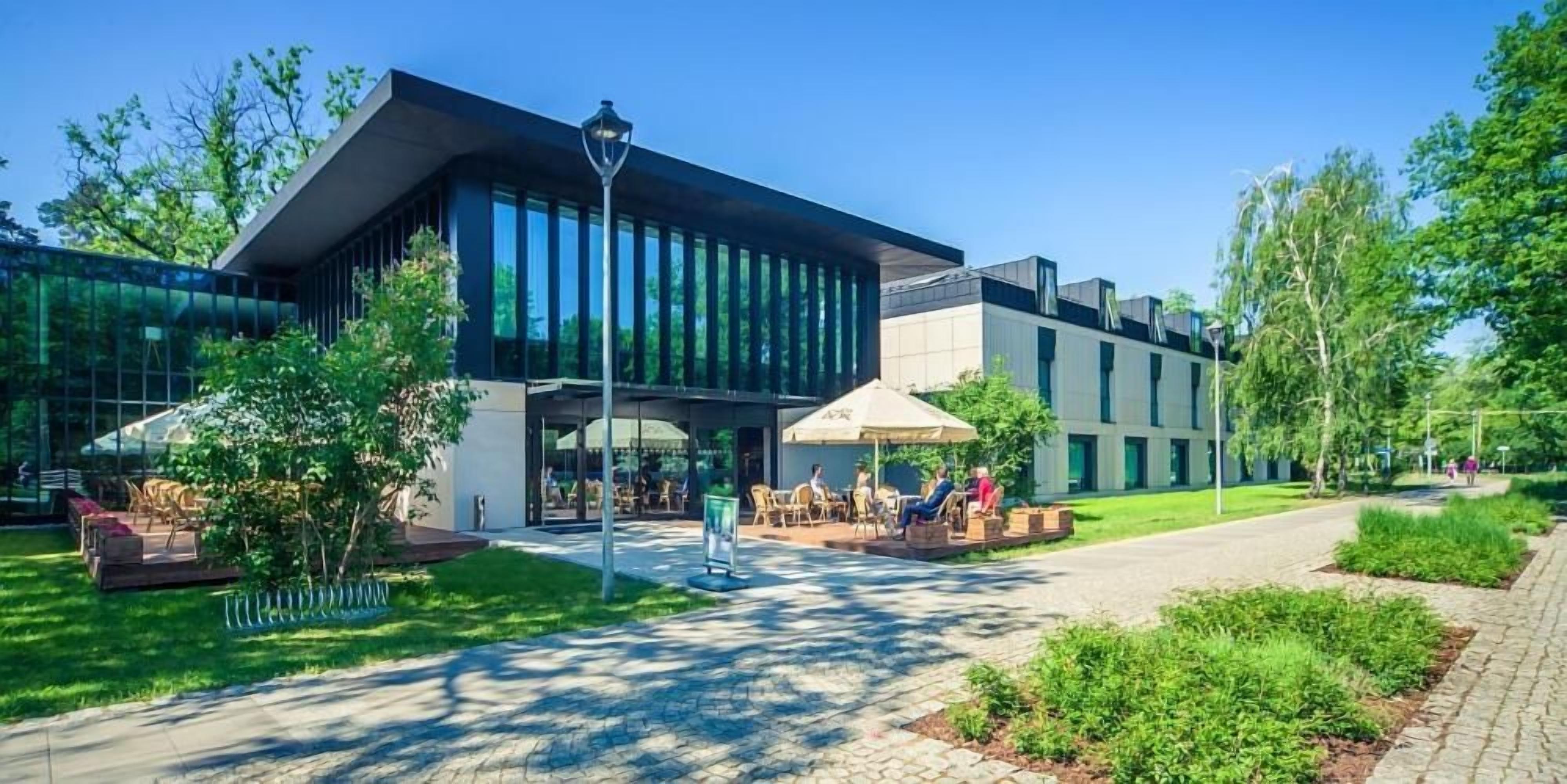 A modern building with a glass facade, outdoor seating area, and a paved walkway.