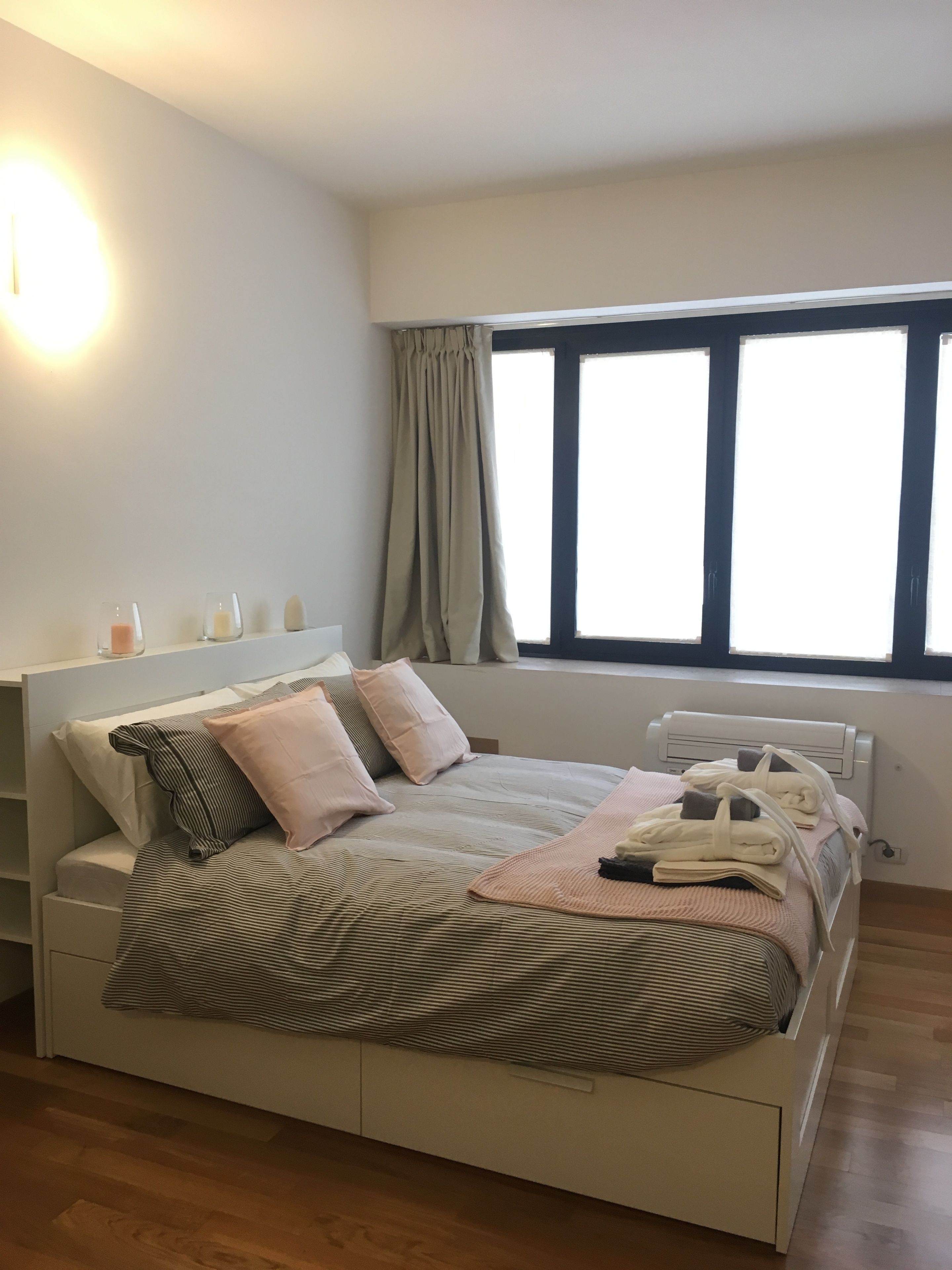 Een slaapkamer met een bed, nachtkastjes, een raam met gordijnen en een radiator.