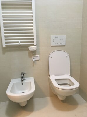 Ein Badezimmer mit Bidet, Waschbecken, einem Fenster mit Jalousien und einem Thermostat an der Wand.