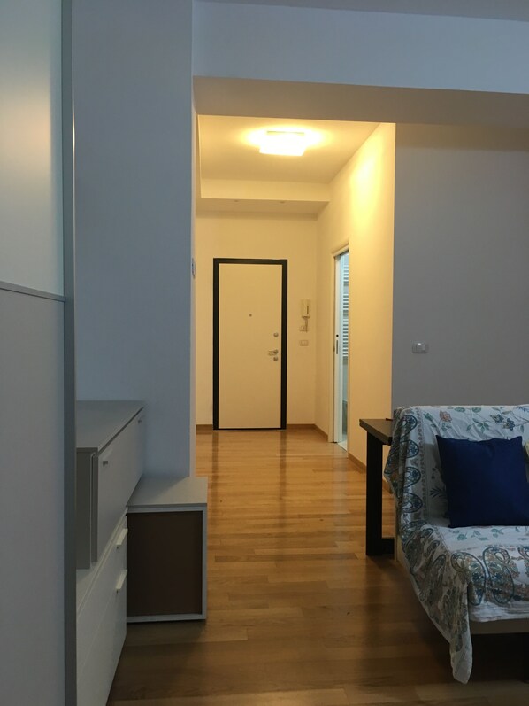 A hallway with a wooden floor, a door at the end, and a sofa with a patterned cover.