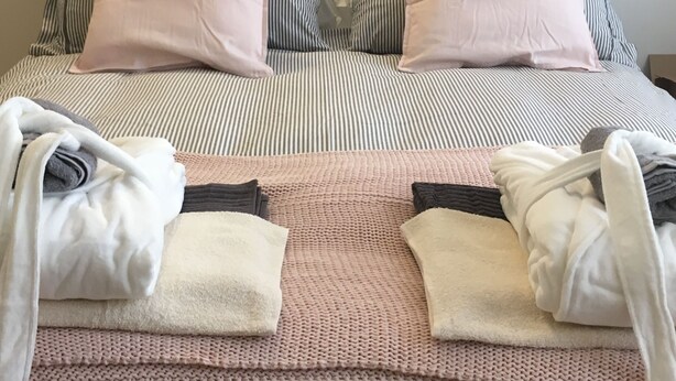 Ein ordentlich bezogenes Bett mit gestreifter Bettwäsche, zwei Kissen und einer rosa Decke.