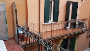 Een balkon met een sierhek van ijzer, een kleine plant in een pot en een raam met groene luiken.