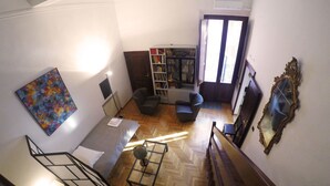Een ruime woonkamer met een visgraatvloer, een boekenkast, een comfortabele fauteuil en een groot schilderij aan de muur.