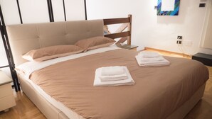 Een net opgemaakt bed met een hoofdbord, nachtkastje en een aan de muur bevestigd kunstwerk.