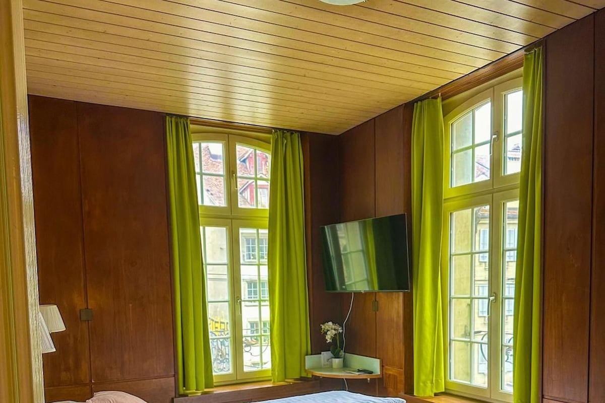 A bedroom with two beds, a television, and large windows with curtains.