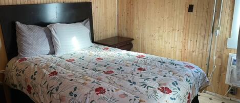 A bed with a floral bedspread, a wooden headboard, and a nightstand with a lamp.