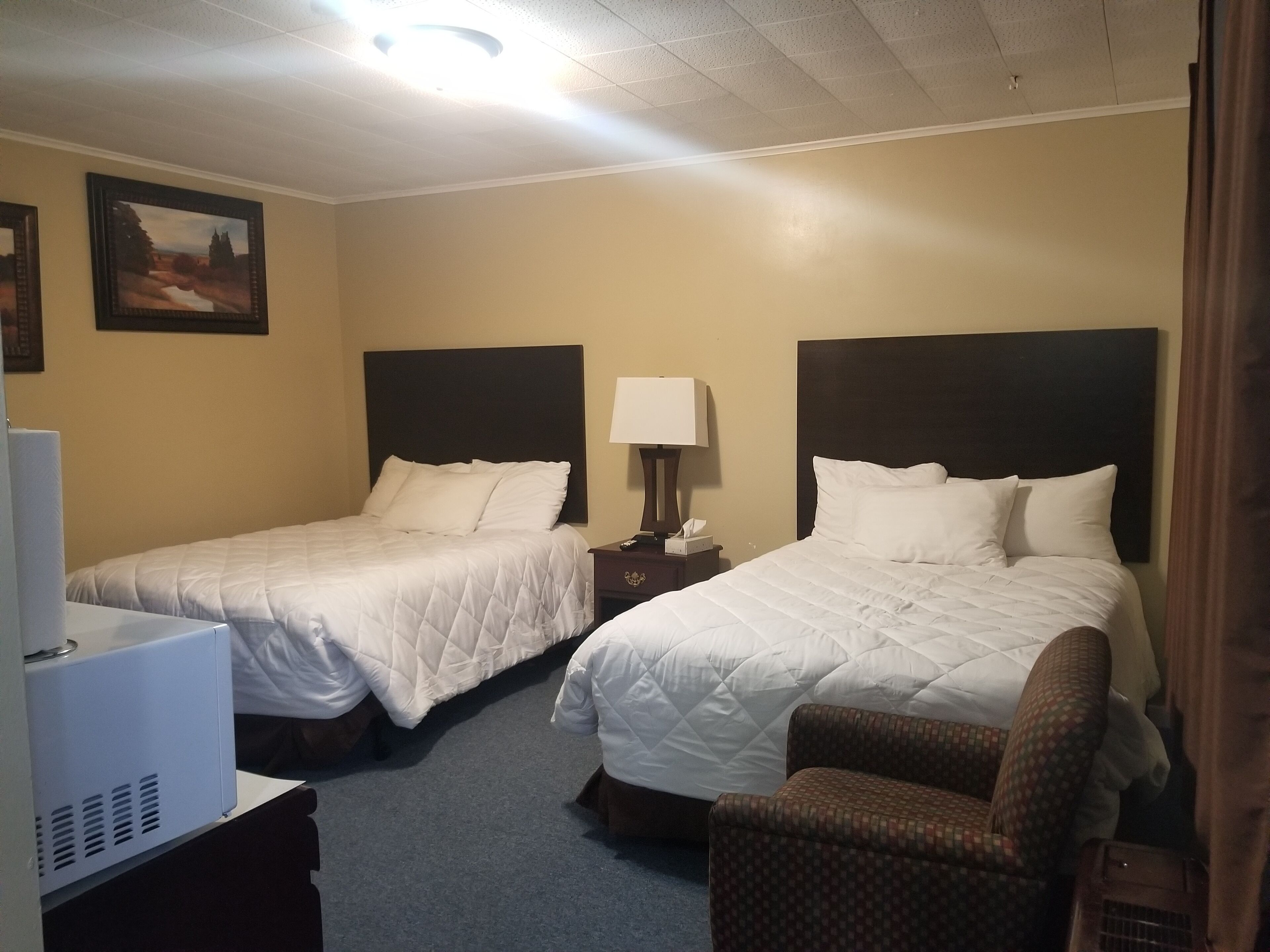 A hotel room with two beds, a desk with a computer, a chair, and a nightstand with a lamp.