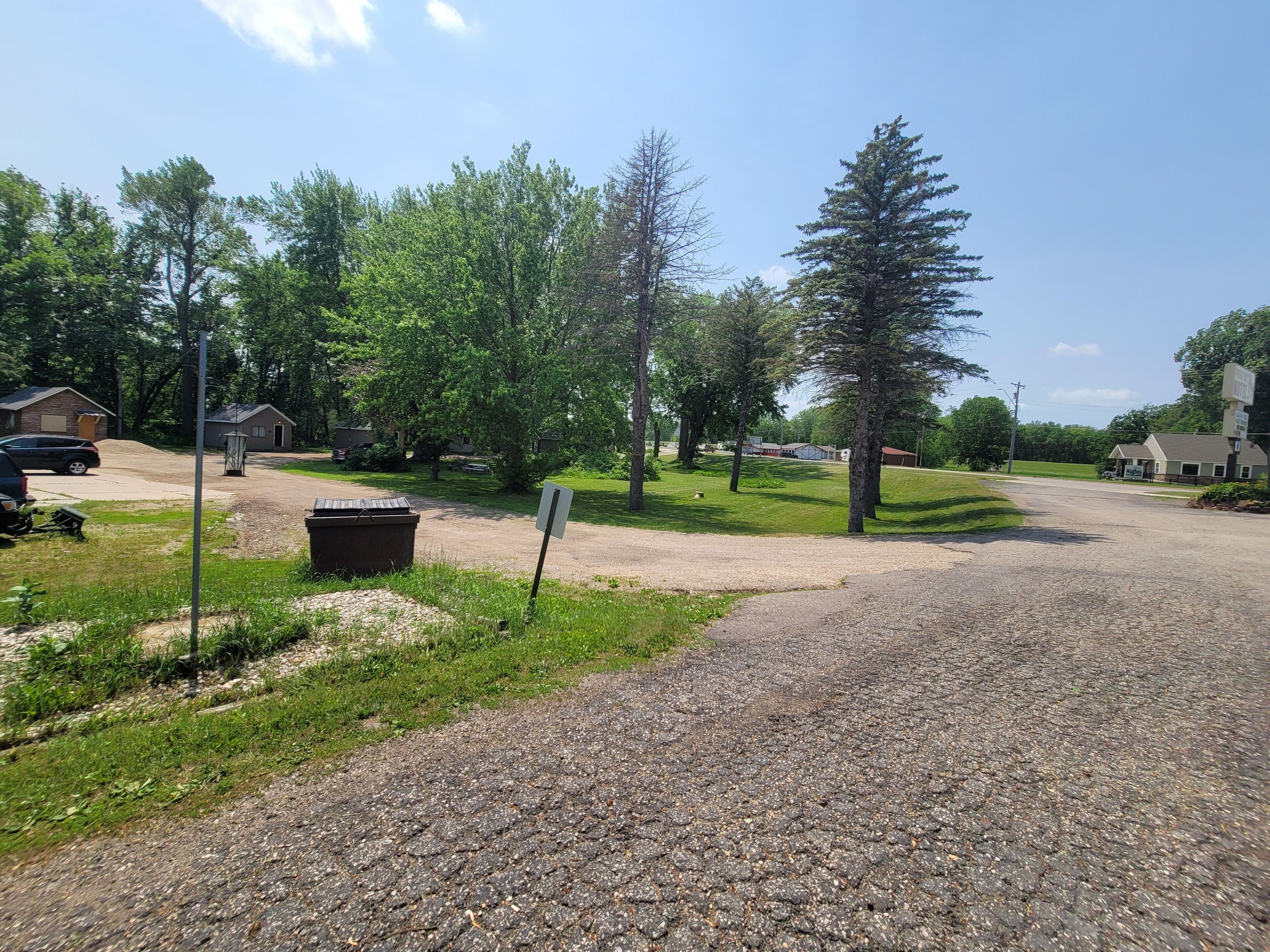 A gravel driveway leading to a building with a signboard, surrounded by trees and a grassy area.