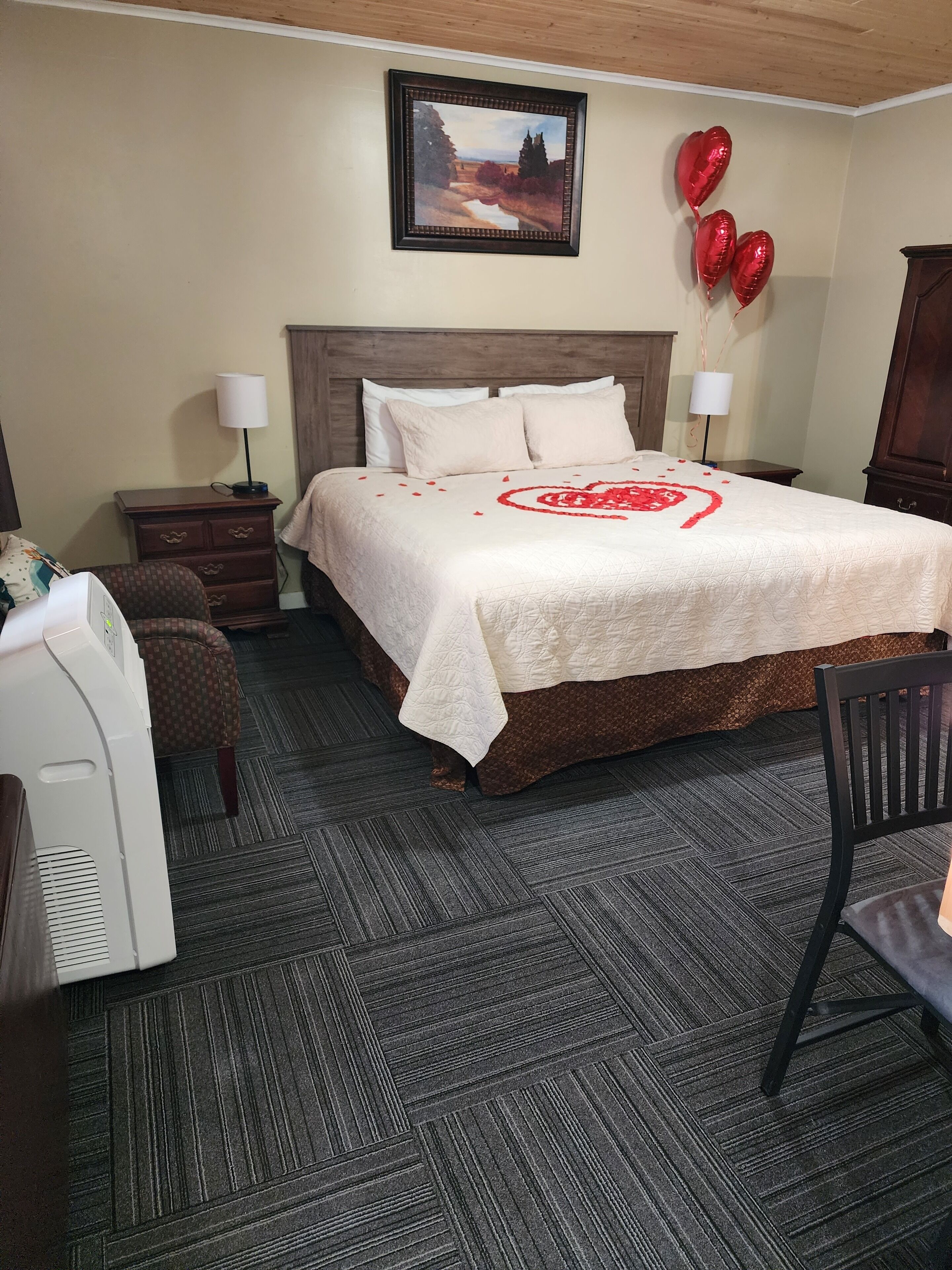 A hotel room with a bed, a desk, a chair, a dresser, and a painting on the wall.