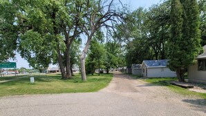A gravel driveway leading to a row of single-story mobile homes with a grassy area and trees. - Fiesta City Motel (Montevideo)