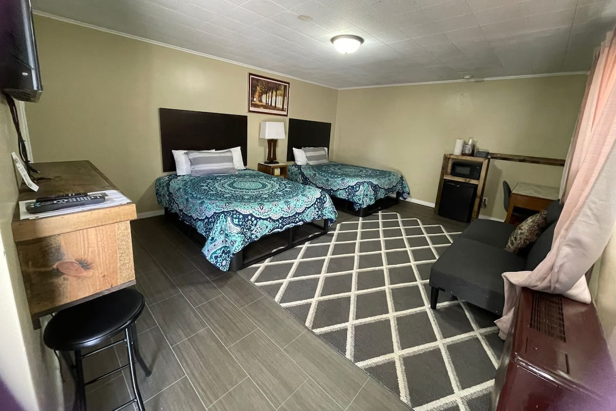 A hotel room with two beds, a desk with a chair, a small table, a TV, and a bathroom.