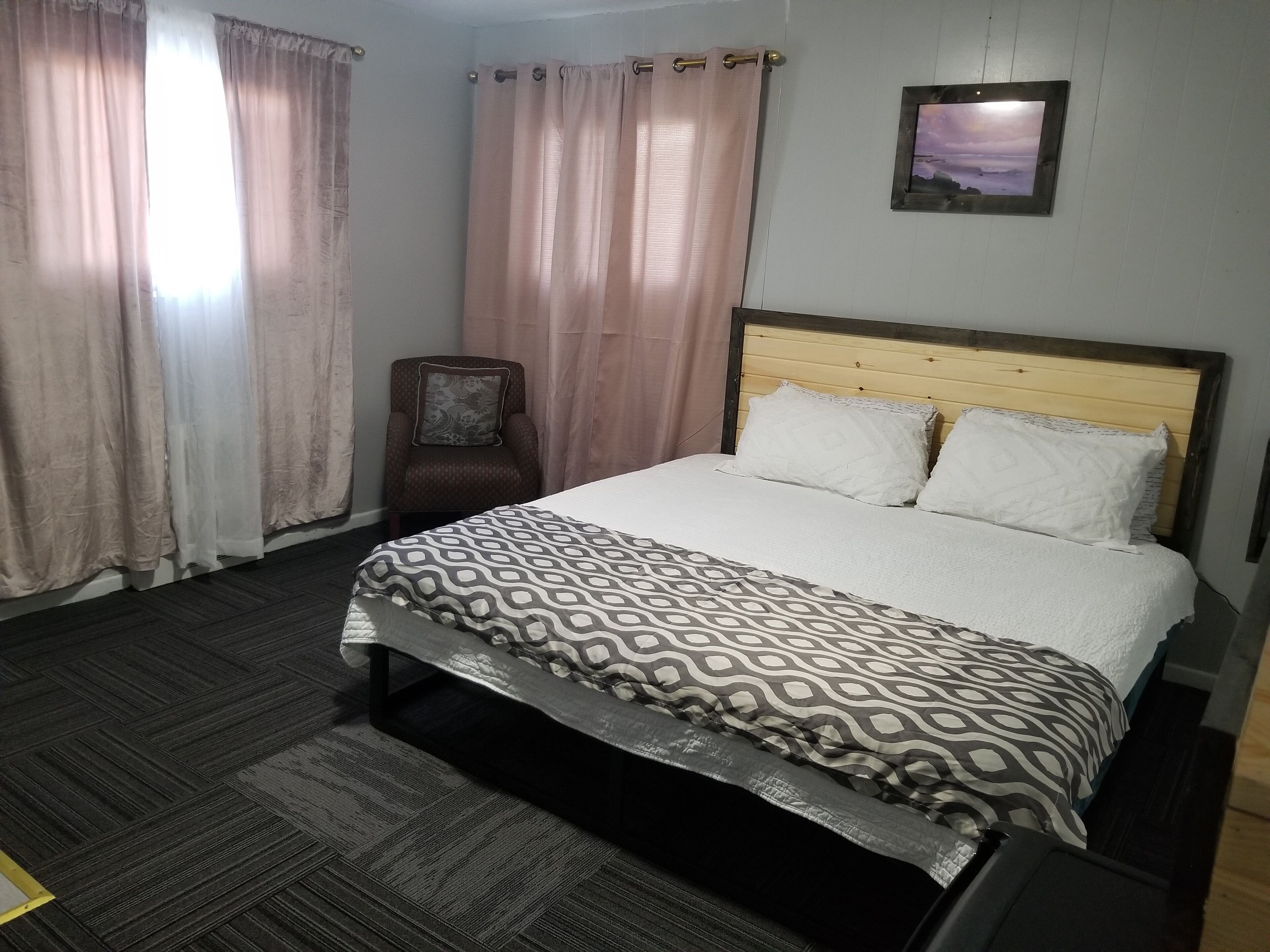 Una habitación de hotel con una cama, una silla y un cuadro en la pared.