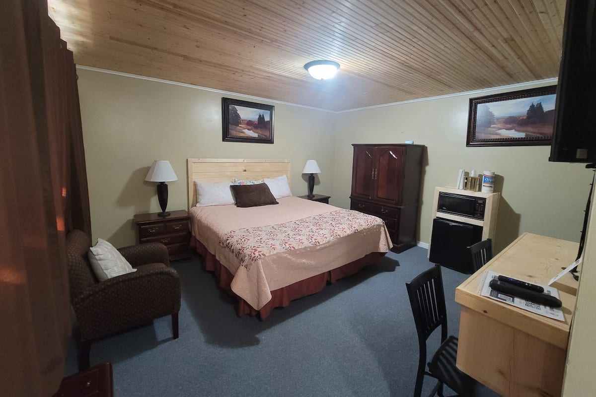 A bedroom with a bed, a wooden wardrobe, a desk with a chair, and two wall-mounted lamps.