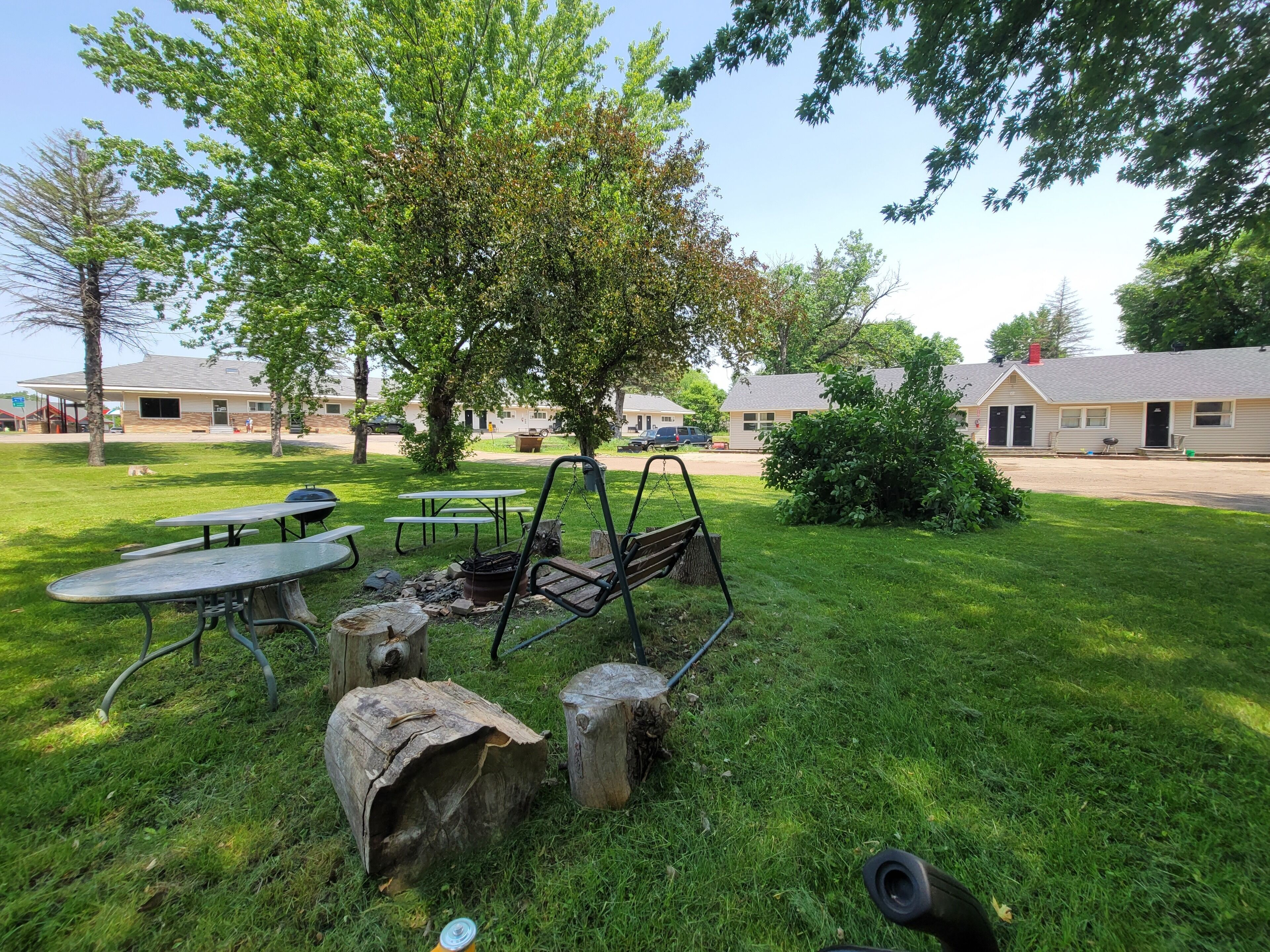 A grassy outdoor area with picnic tables, a swing set, and a small fire pit.