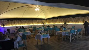 An indoor dining area with tables covered in white tablecloths and blue chairs, under a large tent-like structure with a bamboo wall. - Le Hublot (Abomey-Calavi)