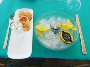 Ein Tisch mit einem weißen Teller Pfannkuchen, einem Glas Milch mit schwarzen Kernen, einer Schüssel Eis mit Zitronenscheiben und einer Marmeladengläschen.