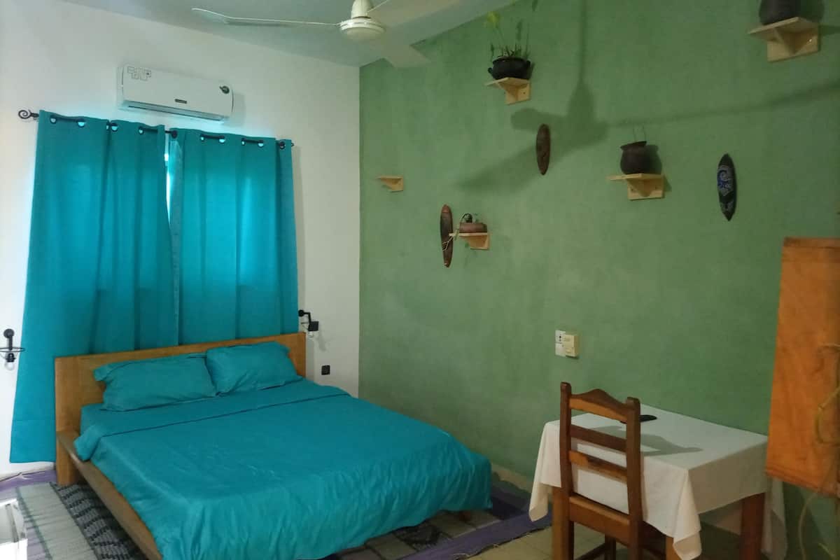 A bedroom with a bed, a chair, a table, and a ceiling fan.