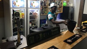 A bar area with a beer tap, a refrigerated display case, and shelves stocked with bottles. - Le Hublot (Abomey-Calavi)