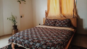 A bedroom with a wooden bed, patterned bedding, a potted plant, and a ceiling fan. - Le Hublot (Abomey-Calavi)
